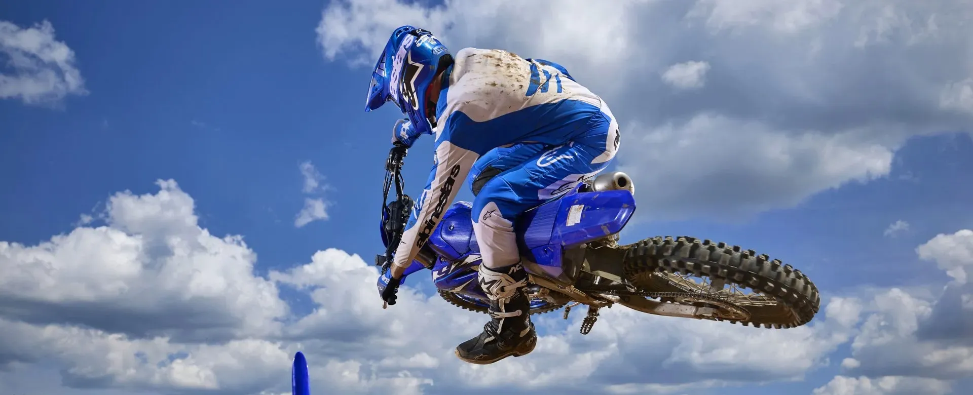 Rider performing a jump on a blue Yamaha dirt bike against a cloudy sky
