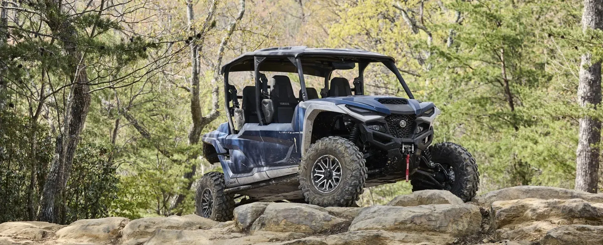 Blue Yamaha Wolverine RMAX4 1000 side-by-side parked on a rocky forest path
