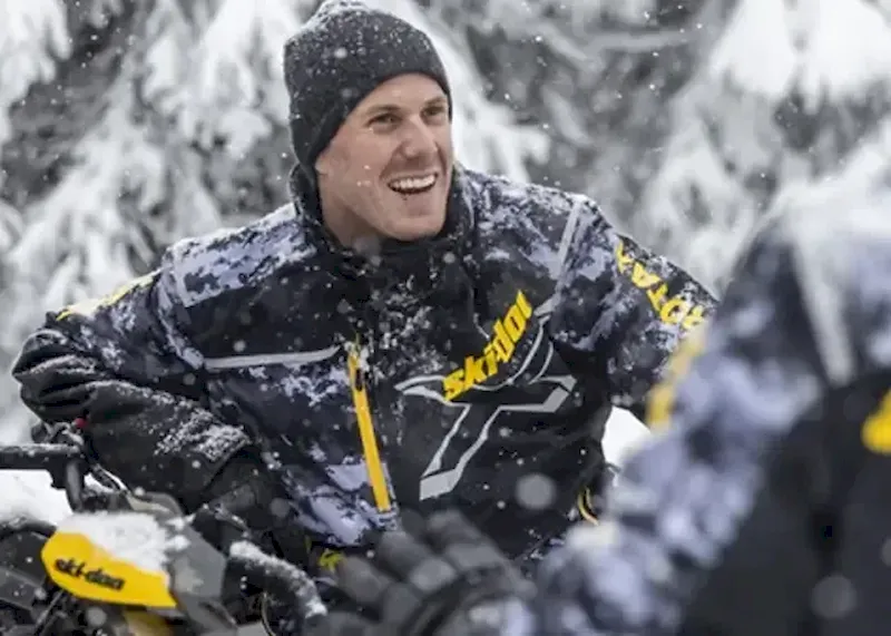 Rider in snowy forest wearing camo snowmobile jacket and riding gear
