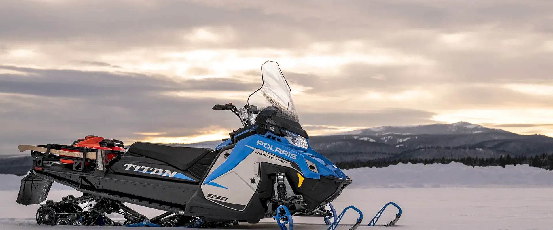 Blue and white Polaris snowmobile parked in a snowy mountain field