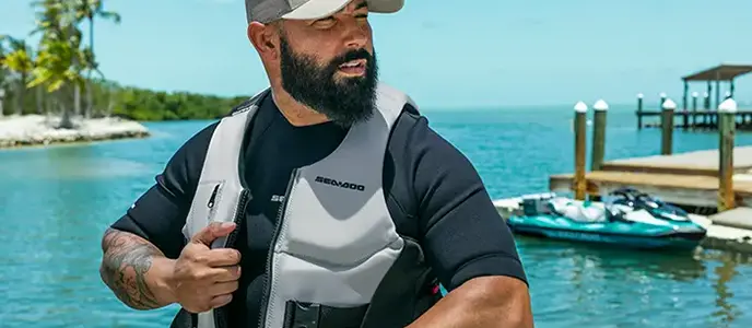 Man in a Sea-Doo life jacket and cap at a tropical waterfront dock